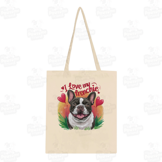 A Tote bag with a cute design featuring a french bulldog smiling surrounded by heart designs, and the phrase "I love my Frenchie". The color of the tote bag is natural