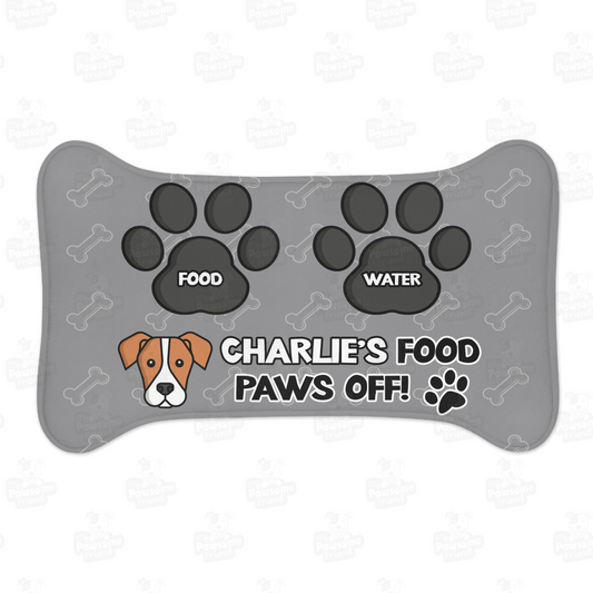 a personalized dog food mat with the a bone shape, two big paws with the words "Food" and "Water" at the top. And the face of a cute dog next to the words "Dog's Food Paws Off!". Color of the pet feeding mat is grey